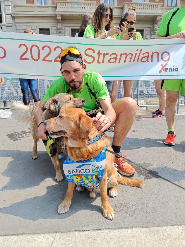 Runner della squadra Xenia con due cani alla Stramilano 2022, dietro lo striscione Xenia