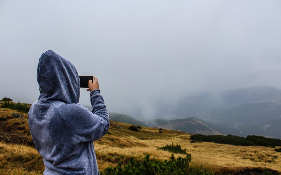 Persona in felpa azzurra che fotografa le colline