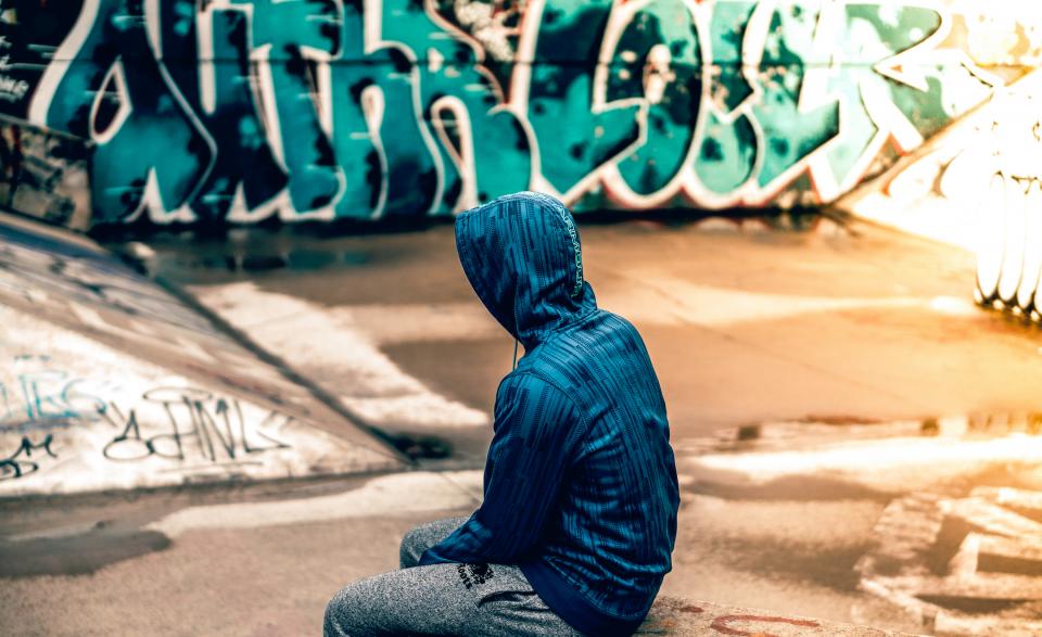 Ragazzo con felpa blu davanti a una parete con graffiti
